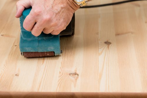 Man holding a belt sander on pine floor or table sanding surface